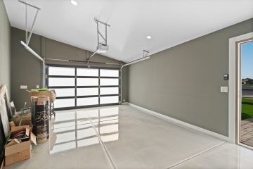 Empty modern garage with glossy floor, overhead storage tracks, and open side door to driveway and lawn